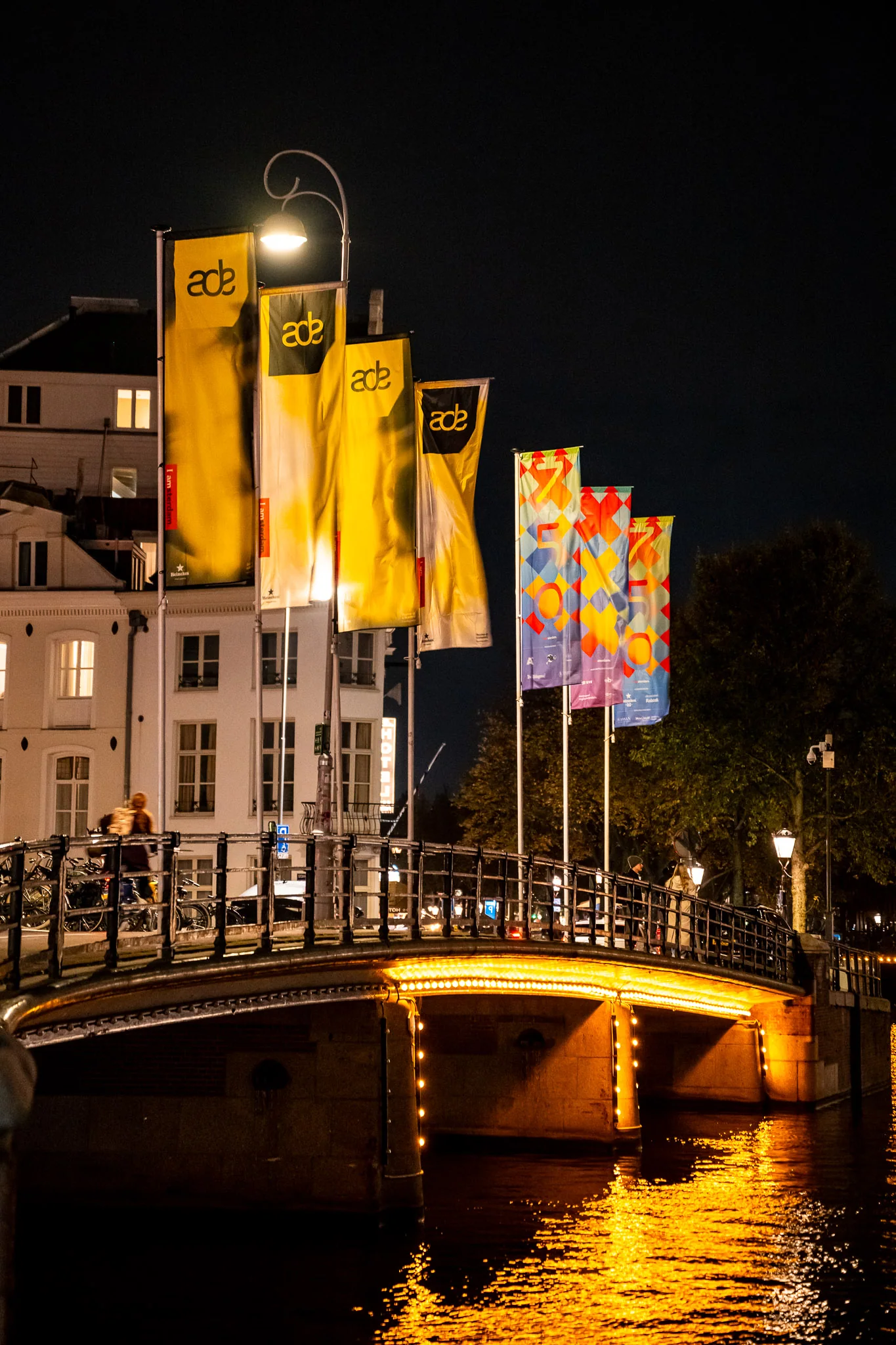 Yellow Amsterdam Dance Event flags above an illuminated canal bridge at night