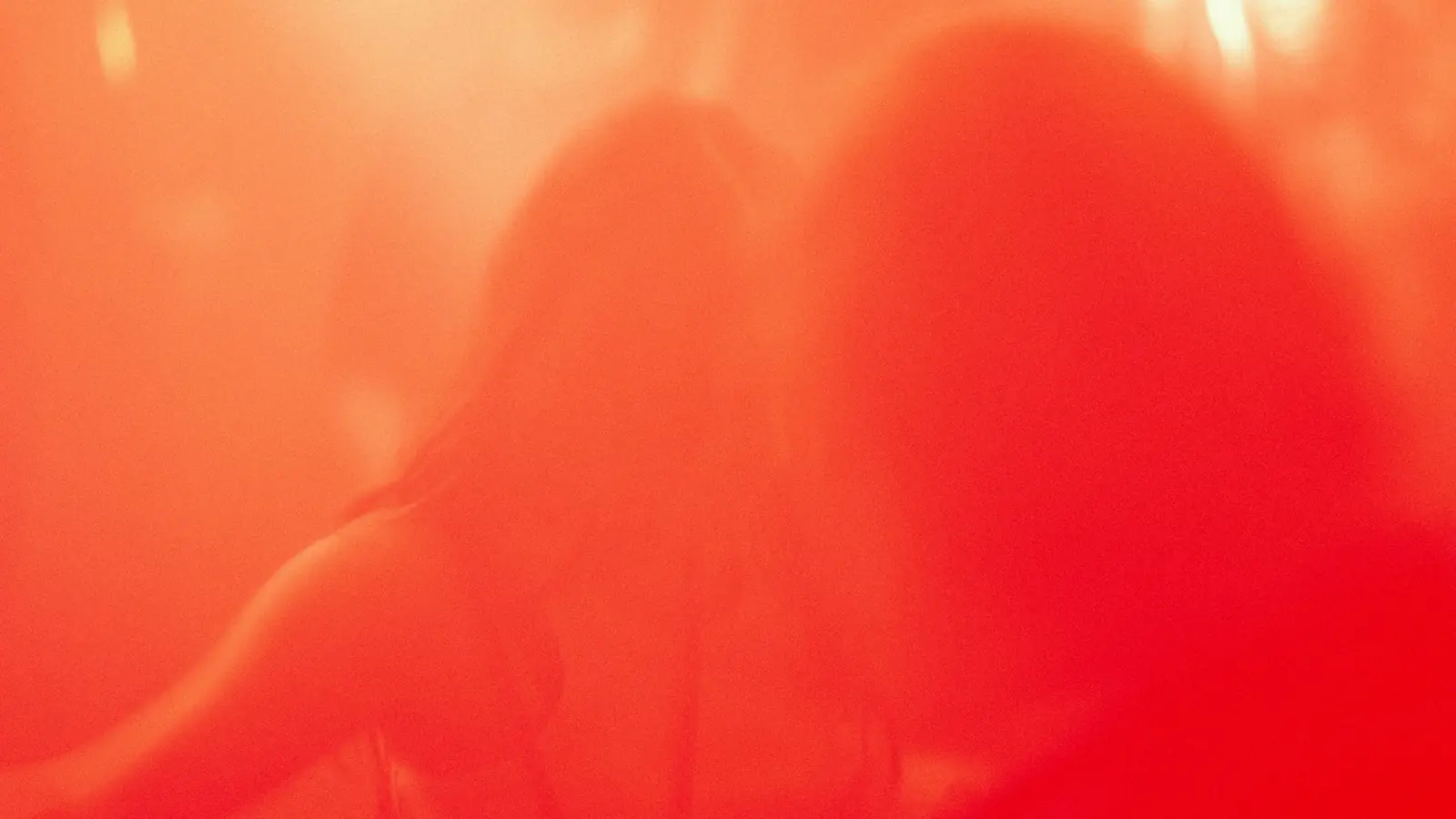 An unresolved, blurred red frame: two silhouetted heads against a wash of red and orange light, no clear shape held long enough to name
