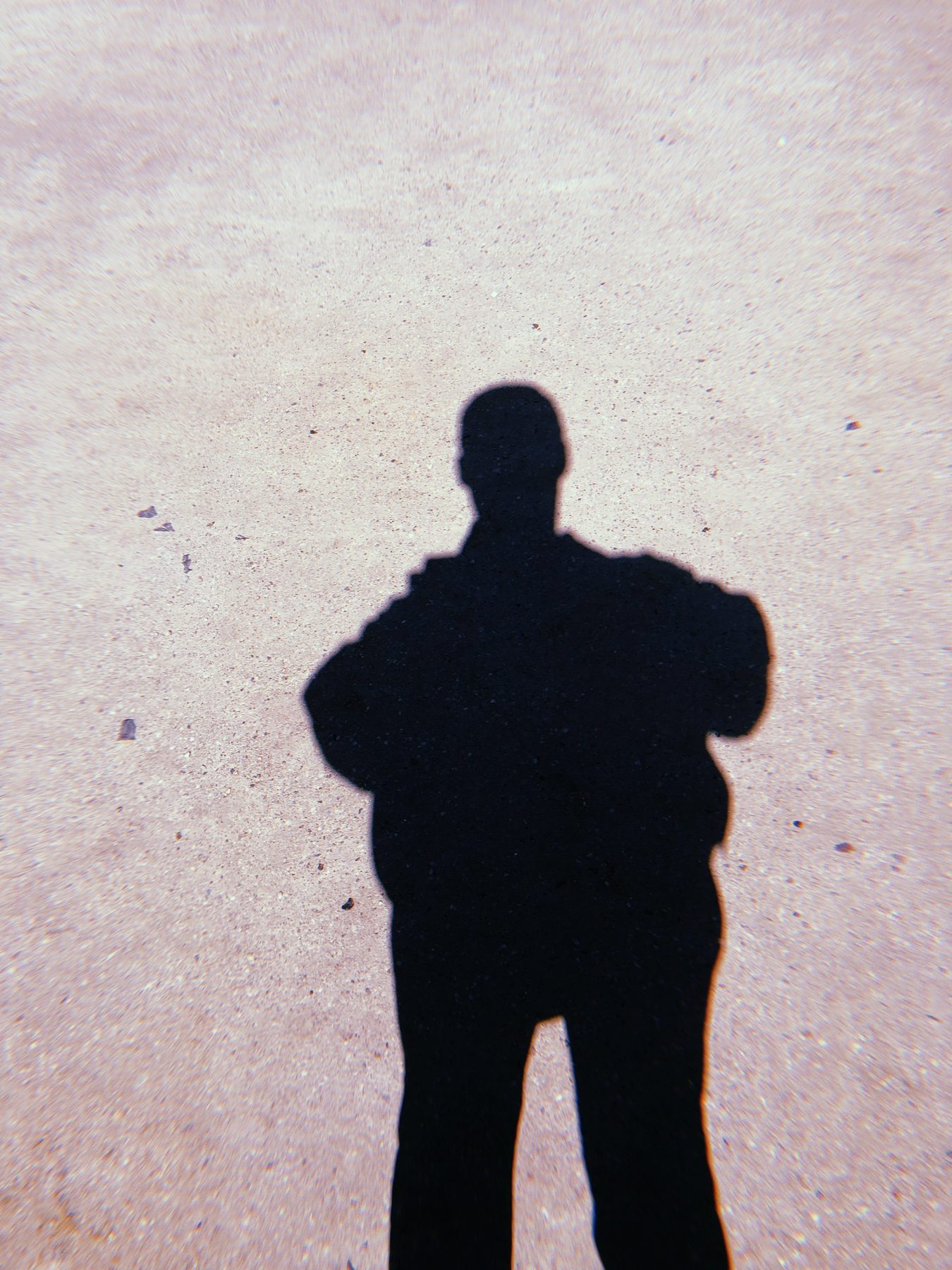 The shadow of a figure cast on pale concrete, arms at their sides, no face visible