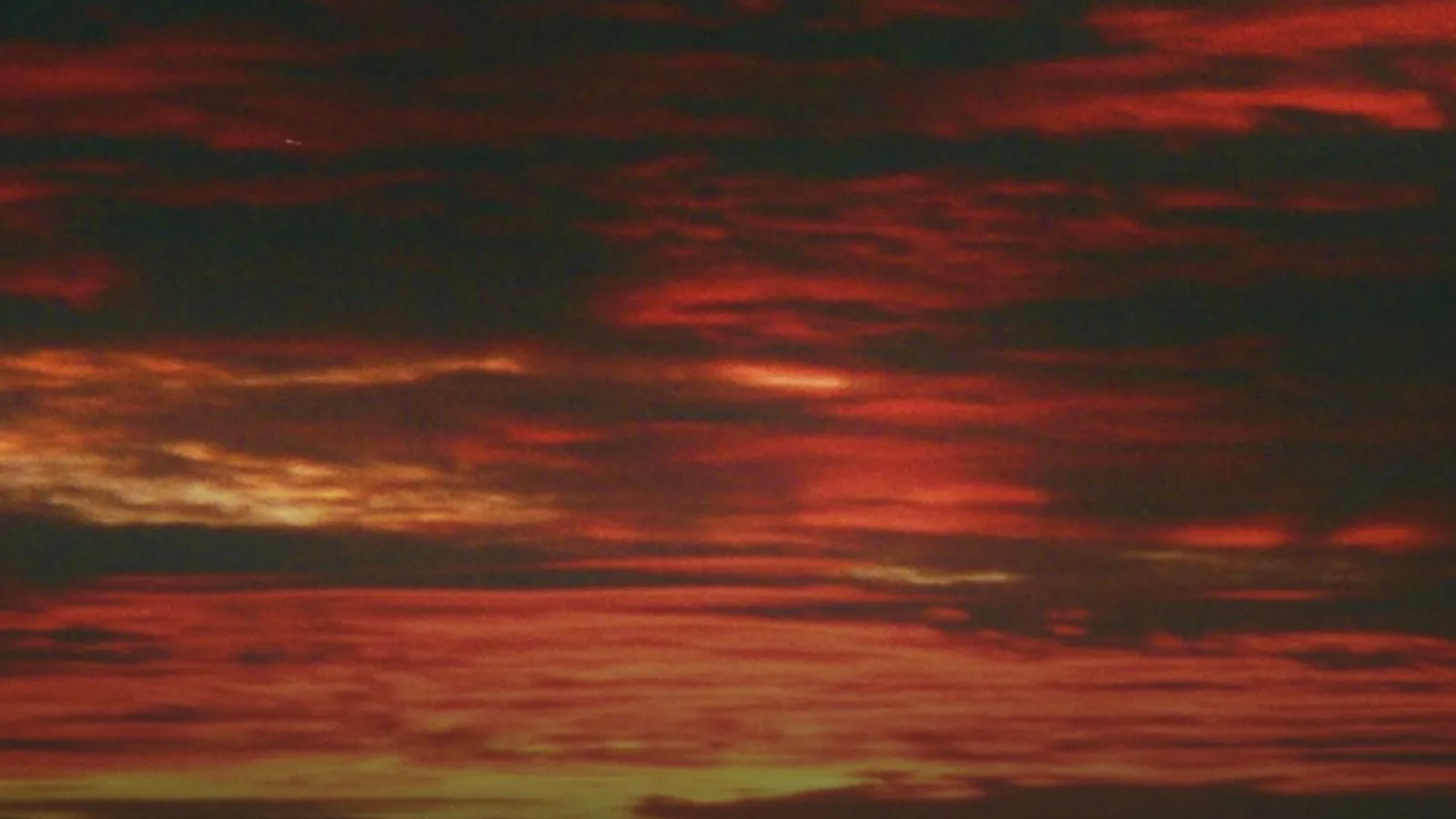 A banded red and orange sunset sky, heavy with film grain, the last light low across the cloud layers